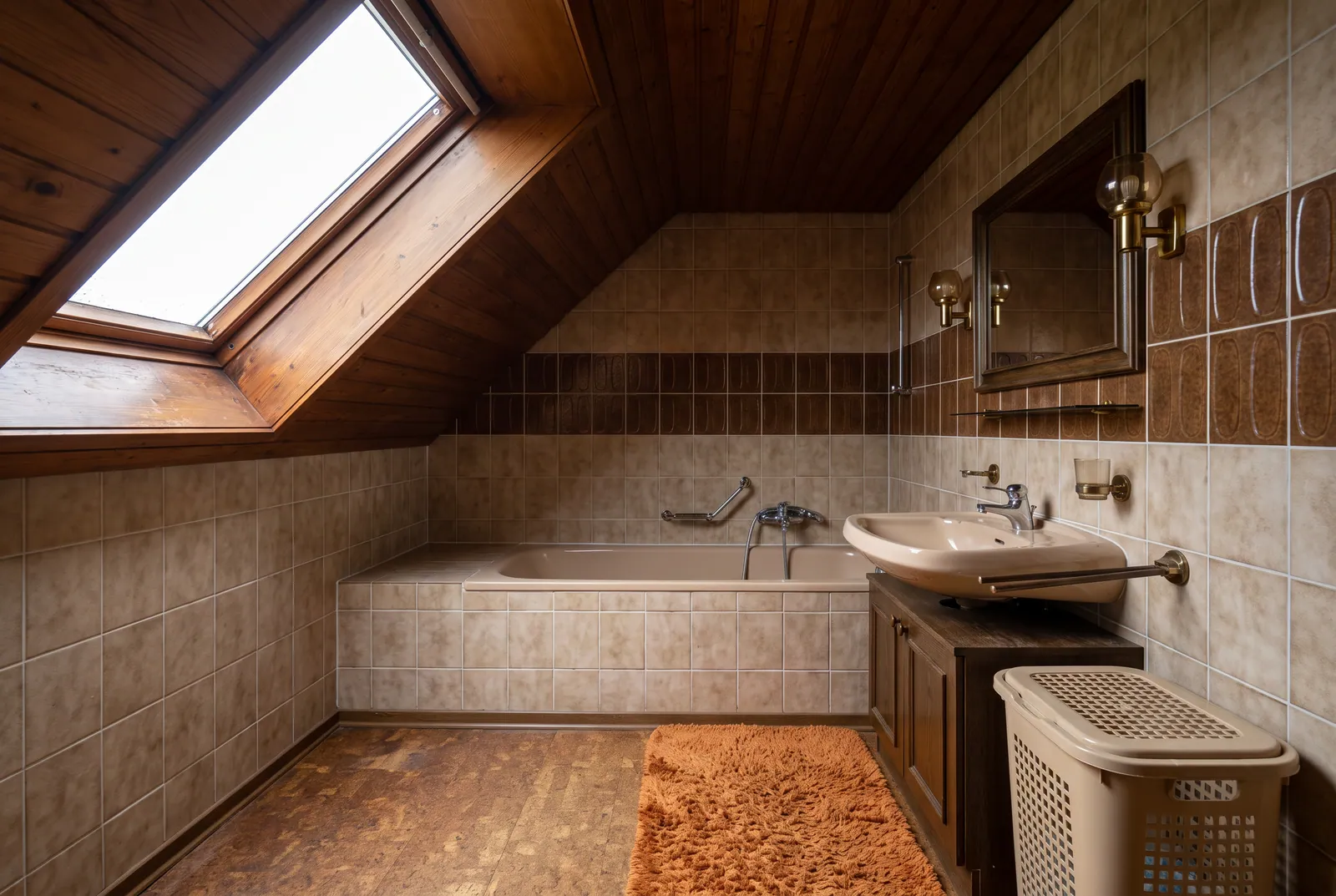 Vorher: Dachbad mit dunkler Holzdecke, beigebraunen Fliesen und eingebauter Wanne