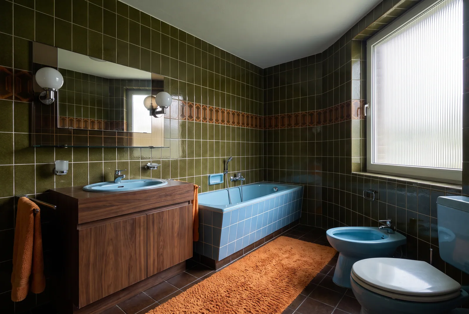 Vorher: Bad mit olivgrünen Fliesen, blauer Wanne, blauem Bidet und orangem Teppich