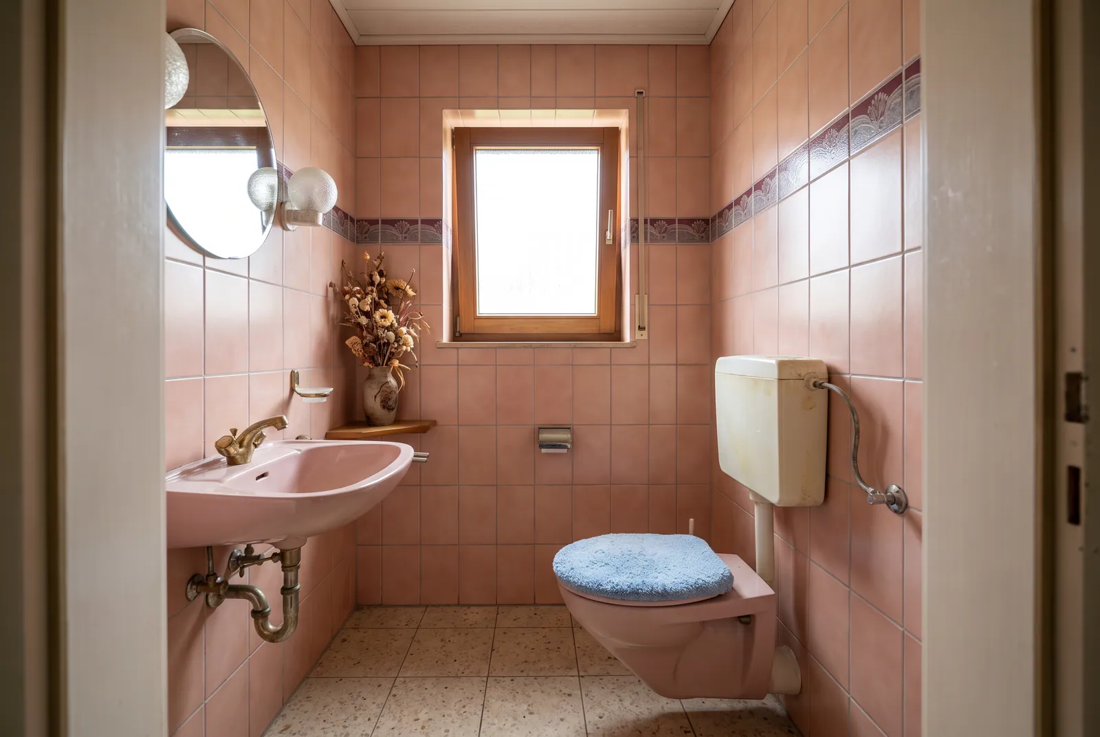 Vorher: Gäste-WC mit lachsrosa Fliesen, rosa Toilette und Spülkasten auf Putz