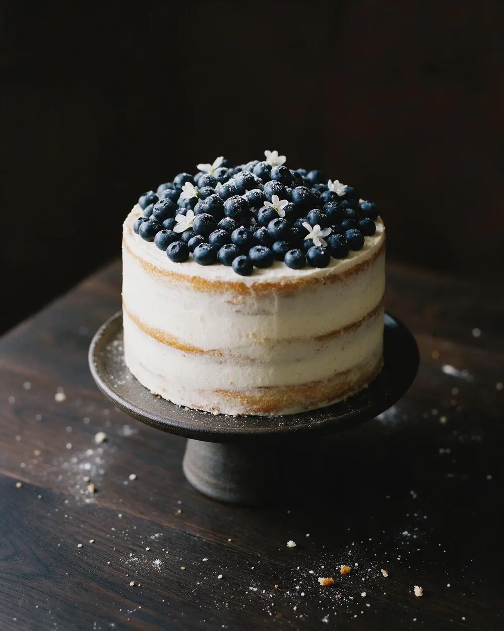 Hohe Heidelbeertorte mit weißer Creme auf dunklem Tortenständer