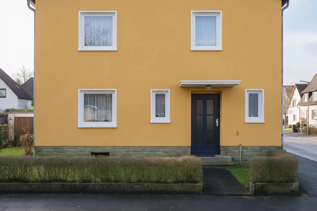 Dieselbe Fassade nach dem Anstrich: warmes Ocker, weiße Fensterrahmen, nachtblaue Haustür